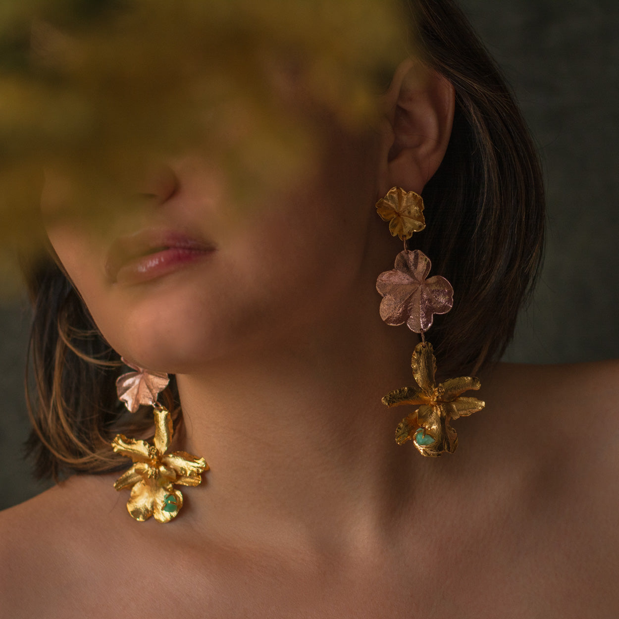 Detalle de los aretes con flores de orquídea y hojas de hiedra en oro, complementados con esmeraldas colombianas